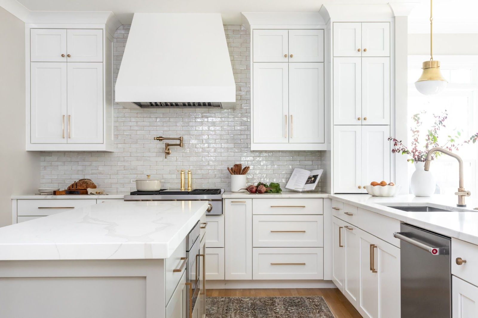 White kitchen with white subway tile, white cabinets, white countertops, and gold hardware. 